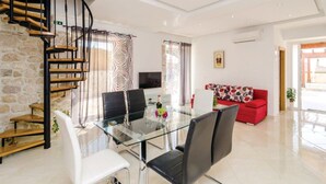 Un salon moderne avec une table à manger en verre, des chaises noires, un canapé rouge, un rideau à motifs zébrés et un escalier en colimaçon.