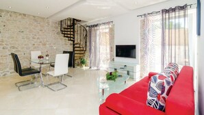 Un salon moderne avec un mur en pierre, un canapé rouge, une table basse en verre et un escalier.