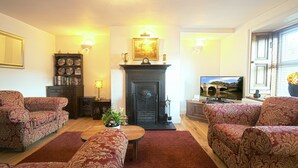 A living room with patterned sofas, a fireplace, a television, and a bookshelf. - Luxury character Cottage in a popular Village location in Central Northumberland (Morpeth)
