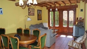 A dining area with a round wooden table and green upholstered chairs, a sofa, and a television in the corner. - Aunt Matea's House for 7 people (Migueláñez)