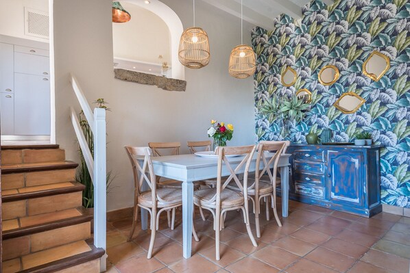 A dining area with a white table and wicker chairs, a blue cabinet with decorative mirrors, and a staircase with wooden steps.