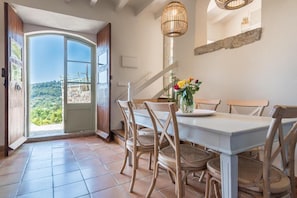 A dining area with a table and chairs, a view through an open door, and a hanging light fixture. - Can Busquera (Sóller)