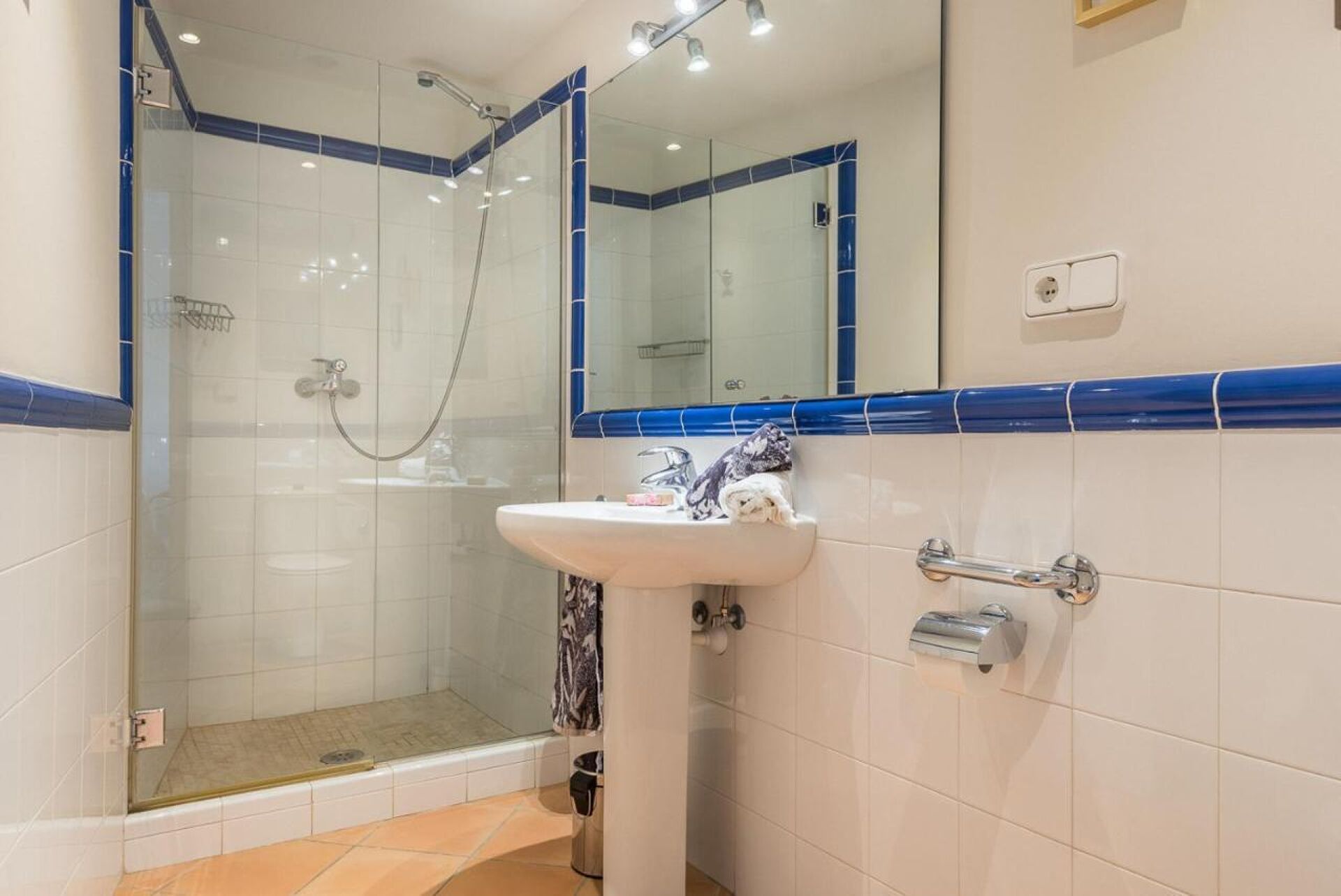 A bathroom with a glass shower enclosure, a sink with a mirror, and a towel rack.