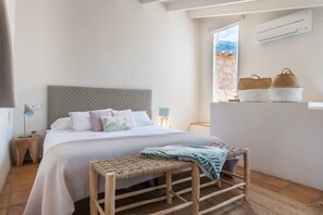 A bedroom with a bed, bedside tables, a bench, and a window with a view. - Can Busquera (Sóller)
