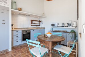 A compact kitchen with a dining area, featuring a wooden table, teal chairs, and a microwave above the counter. - Can Busquera (Sóller)