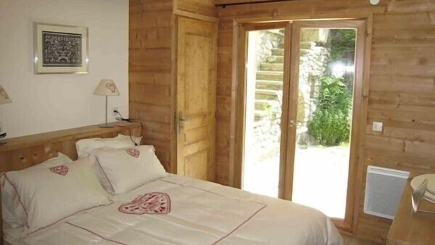 A wooden room with a bed, a door leading to a balcony, and a framed picture on the wall.