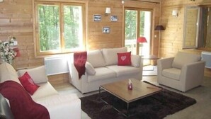 A log cabin interior with a sofa set, a coffee table, and a lamp.
