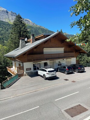 A wooden building with a garage, a staircase, and a parking area with cars. - Luxury 80 sqm 3 bedroom Ski / summer apartment in centre of village (Les Contamines-Montjoie)