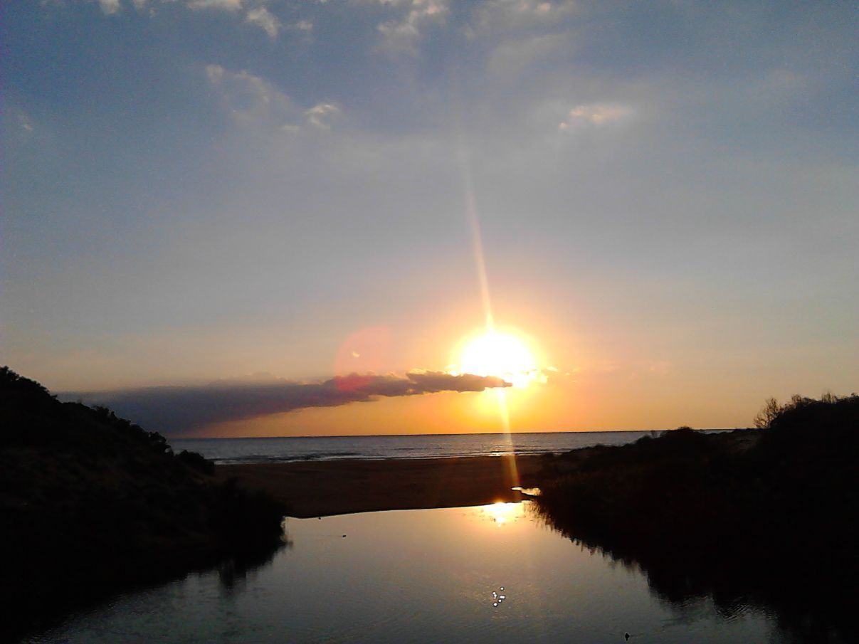A sunset over a calm body of water with a beach in the foreground.