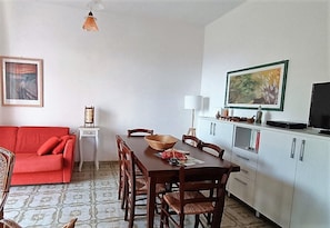Ein Essbereich mit Holztisch und -stühlen, einer roten Couch, einem weißen Schrank mit Fernseher und einem Bild an der Wand.
