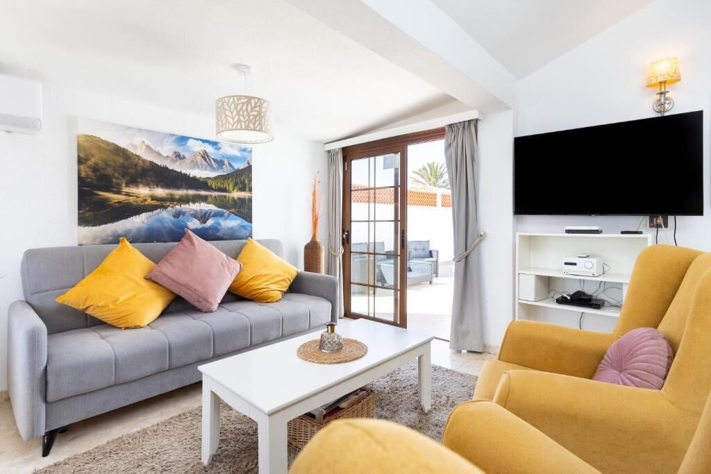 A living room with a sofa, armchair, coffee table, TV, and a painting of a mountain landscape.
