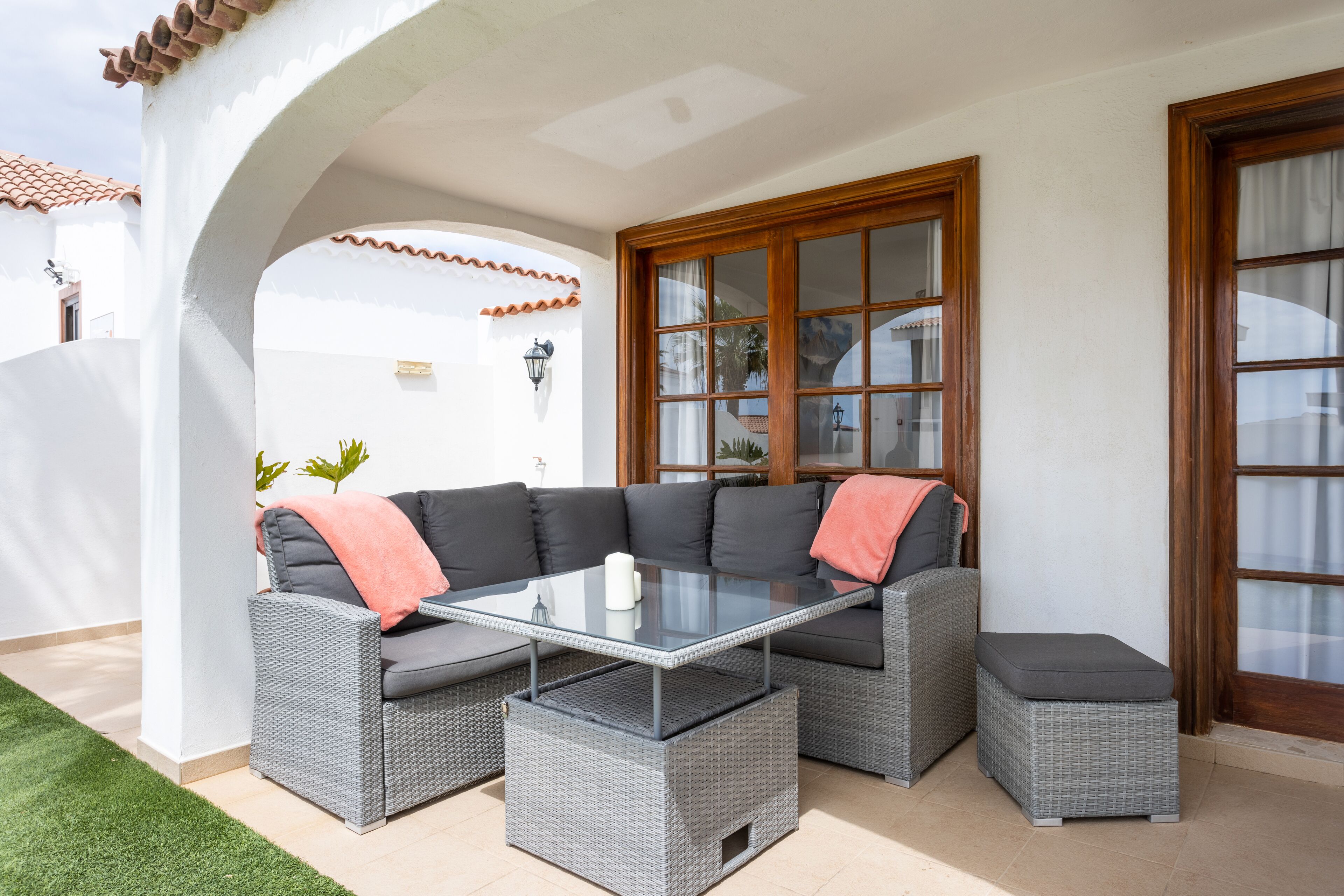 A patio with a glass-top table, grey wicker furniture, and a wooden door.