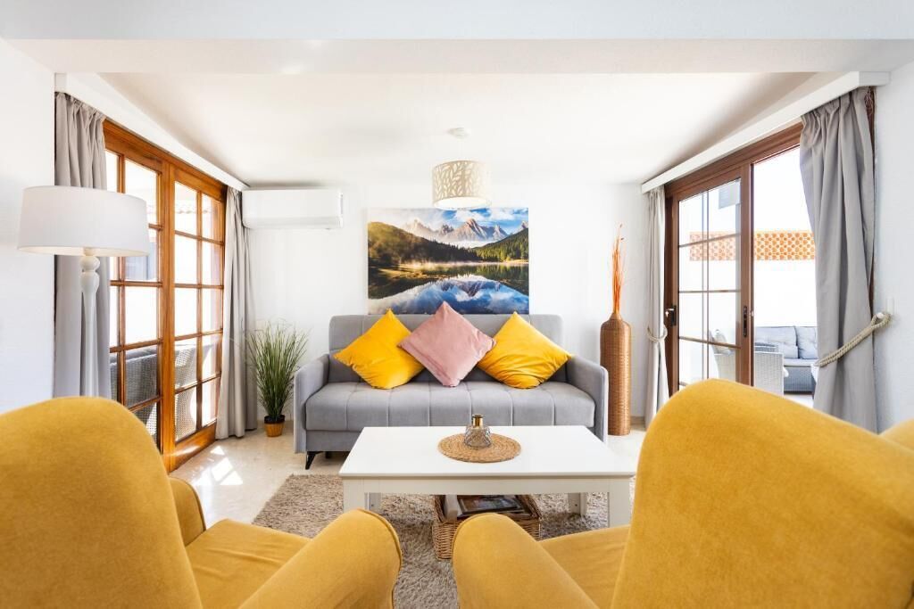 A living room with a sofa, yellow chairs, a coffee table, a painting, and a lamp.