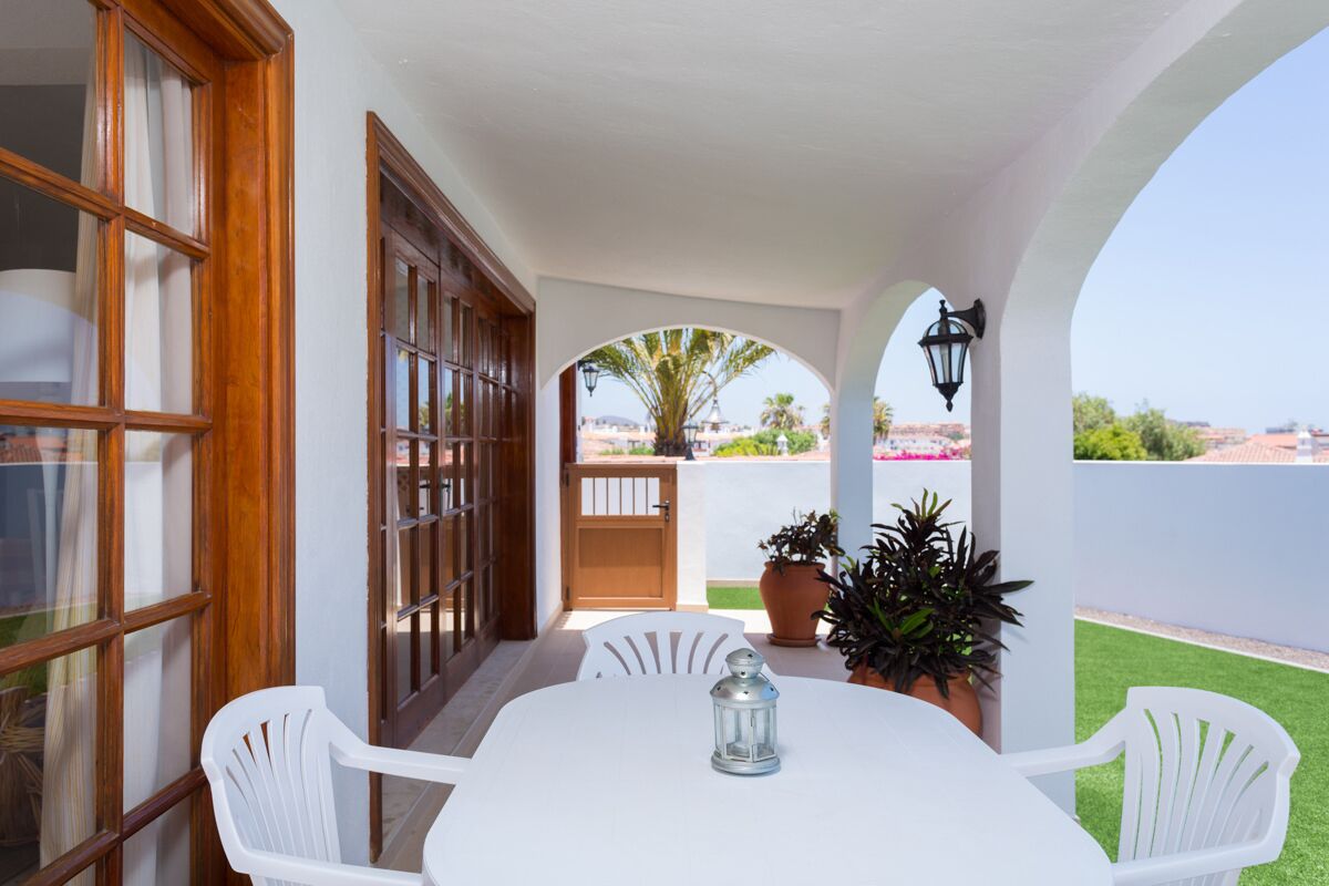 Un patio con mesa y sillas blancas, plantas en macetas y vistas de la ciudad.