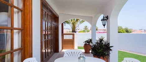 Un patio con mesa y sillas blancas, plantas en macetas y vistas de la ciudad.