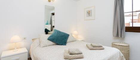 Un dormitorio ordenado con una cama, dos mesitas de noche, un espejo, un cuadro en la pared y una ventana con cortinas.