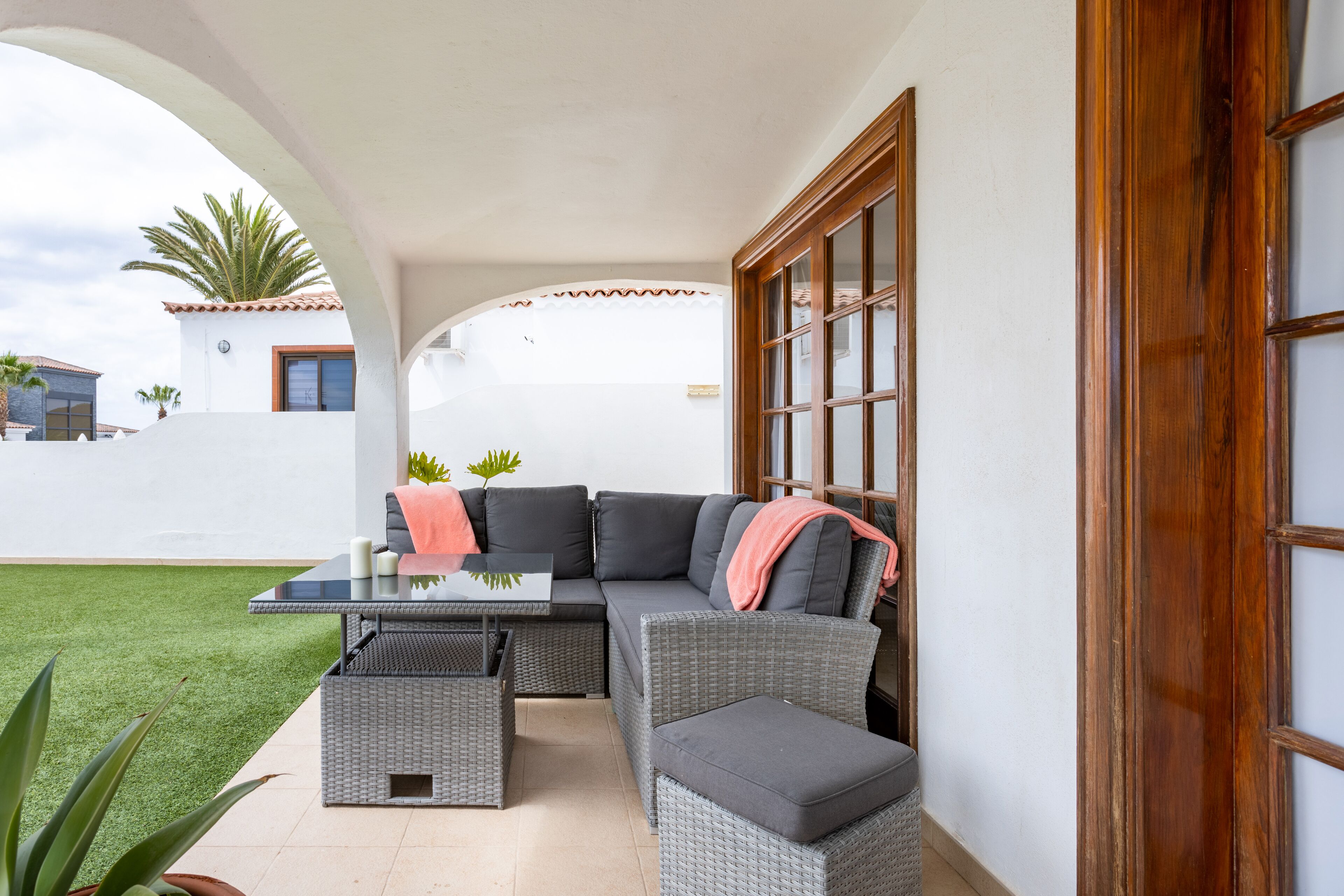 A covered outdoor seating area with a wicker sofa, a glass-top table, and a small table.