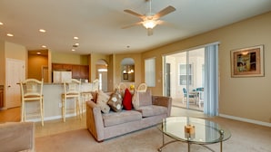 A spacious living area with a glass coffee table, a beige sofa, and a ceiling fan. - Spacious Exec Villa With Large Private Pool. Stunning Golf Course and Lake Views (Davenport)