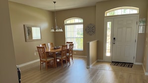 A spacious dining area with a wooden table and chairs, a chandelier, and a large window with blinds. - Spacious Exec Villa With Large Private Pool. Stunning Golf Course and Lake Views (Davenport)