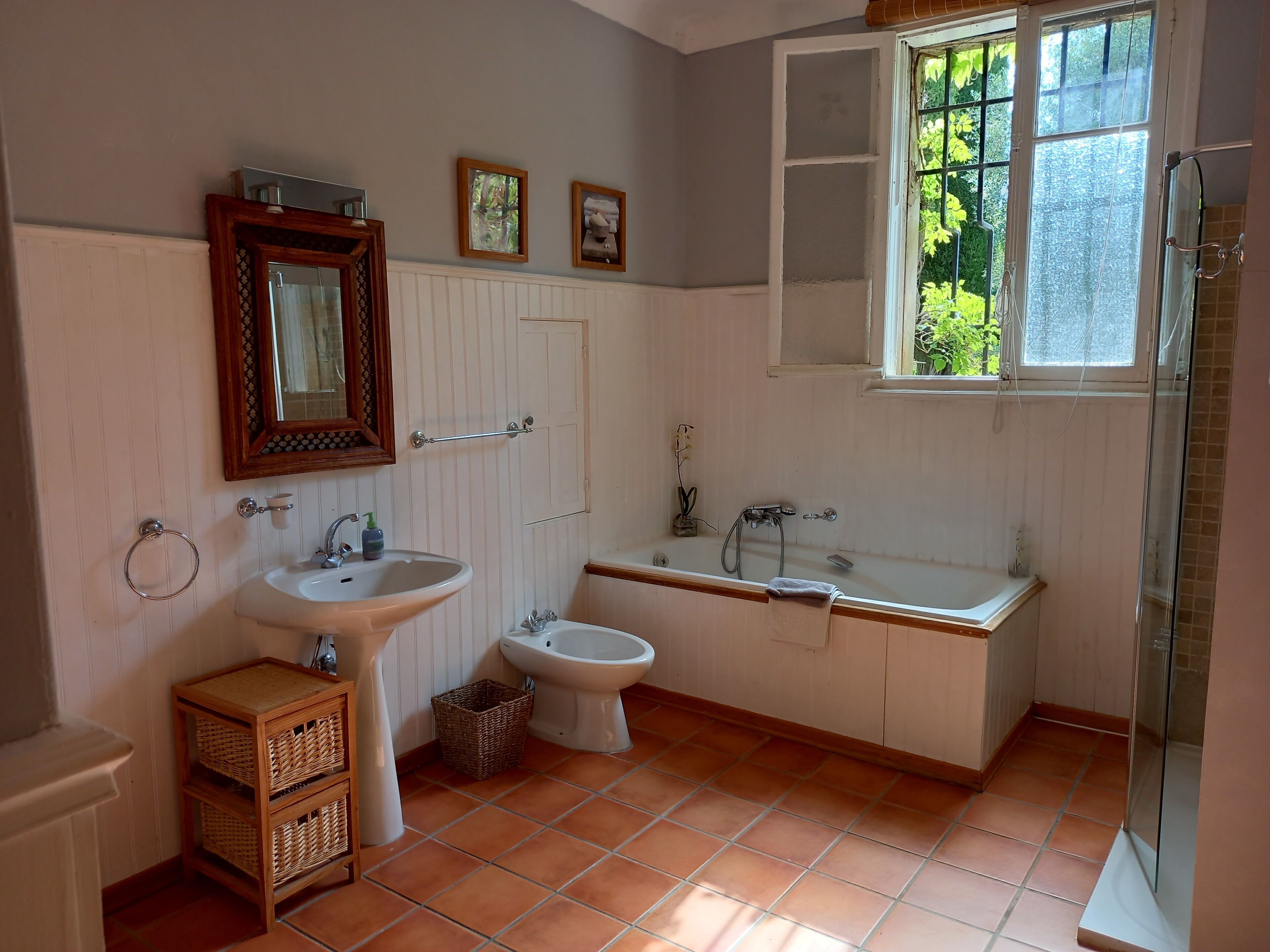A bathroom with a sink, bidet, bathtub, and a window with a view of greenery.