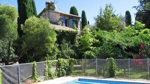 A swimming pool with a stone building in the background, surrounded by lush greenery and a fence. - Lovely Old Stone Bastide With Private Pool, Short Drive To Beach (Vence)