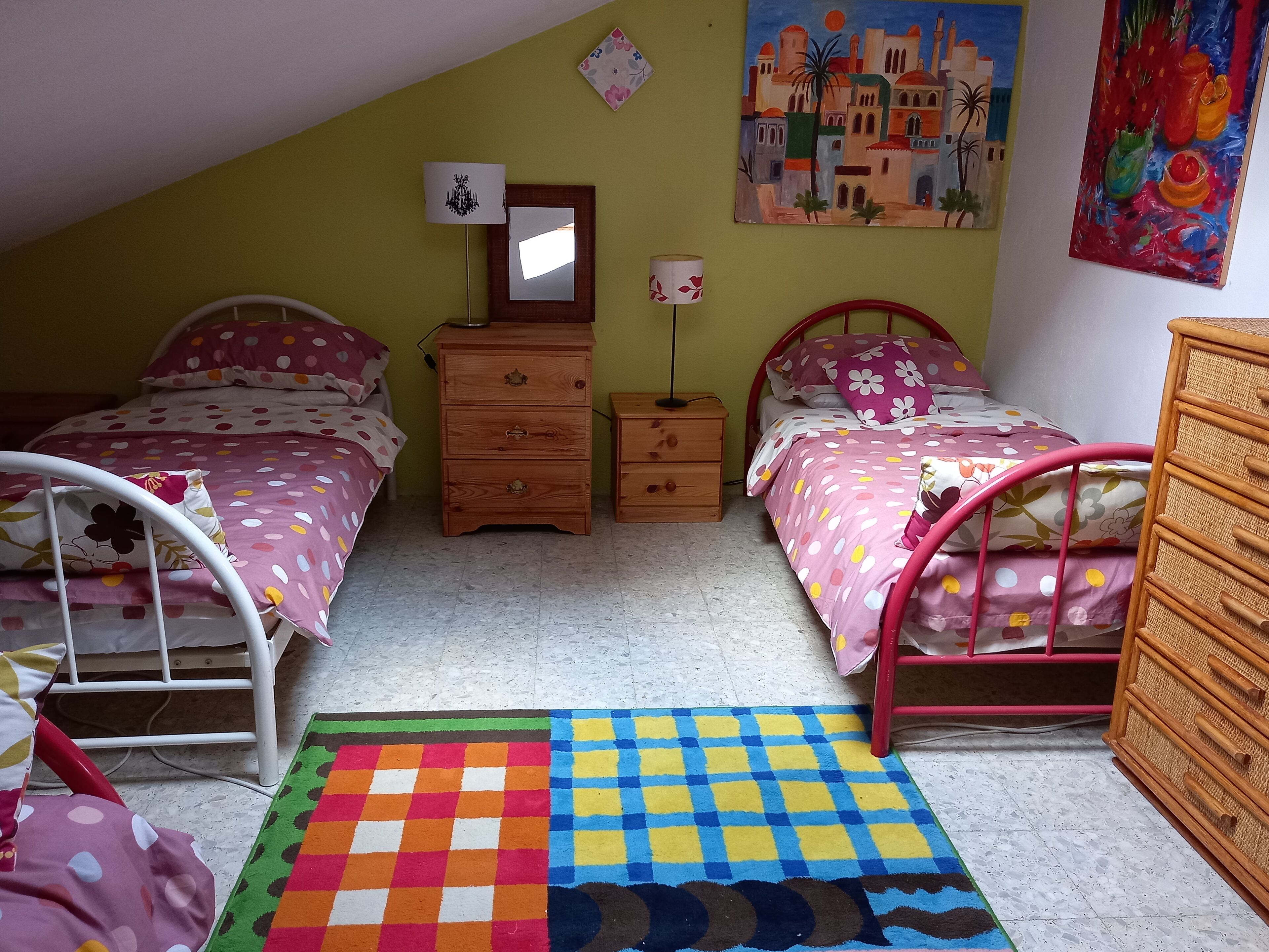 A bedroom with two beds, a dresser, a nightstand, and a colorful rug.