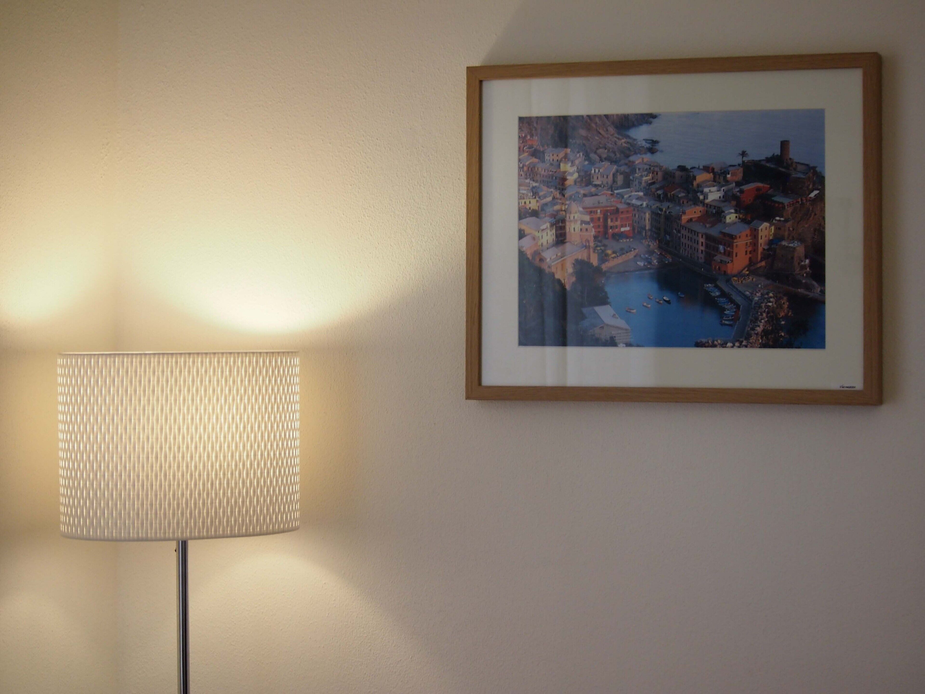 A framed coastal town painting on a wall, a lamp, and a textured wall.