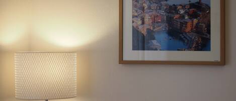 A framed coastal town painting on a wall, a lamp, and a textured wall.