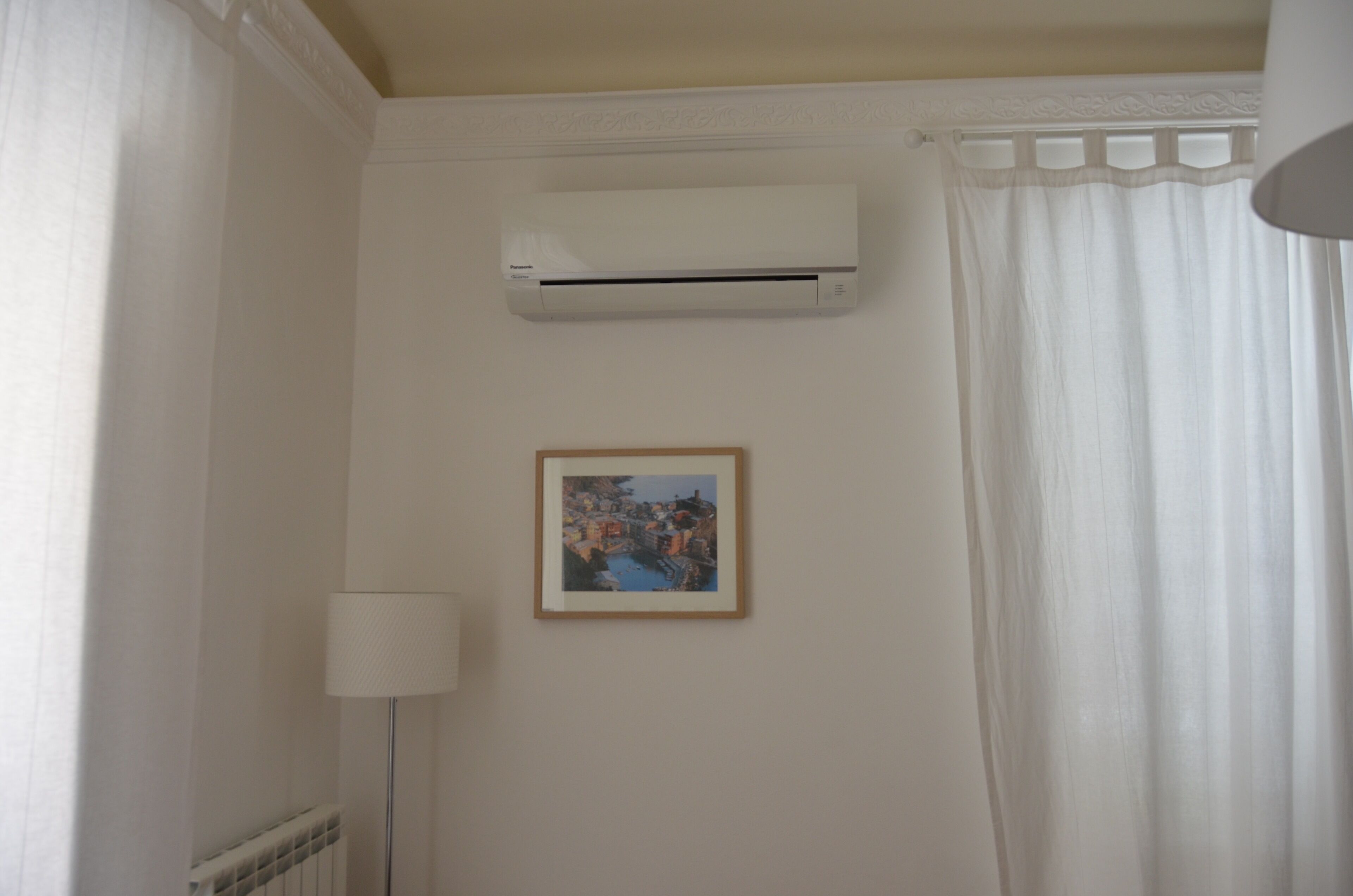 Ein Badezimmer mit einer weißen Klimaanlage, einem gerahmten Bild an der Wand und einem weißen Vorhang.