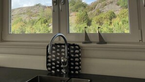 A kitchen with a double sink, a window with a view of a mountainous landscape, and a decorative item on the windowsill. - Wonderful house in Strömstad! (Strömstad)