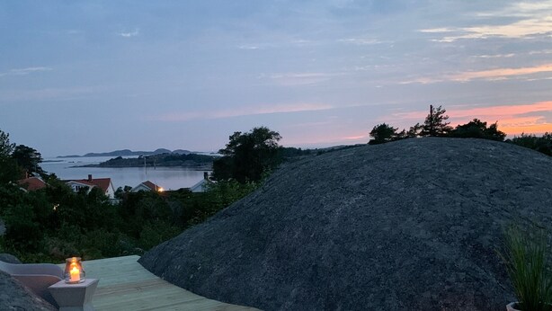 A wooden deck with a stone wall and a view of the sea at dusk. - Wonderful house in Strömstad! (Strömstad)