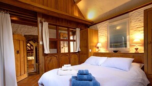 Une pièce en bois avec un lit, des rideaux blancs et une fenêtre donnant sur un paysage agréable.