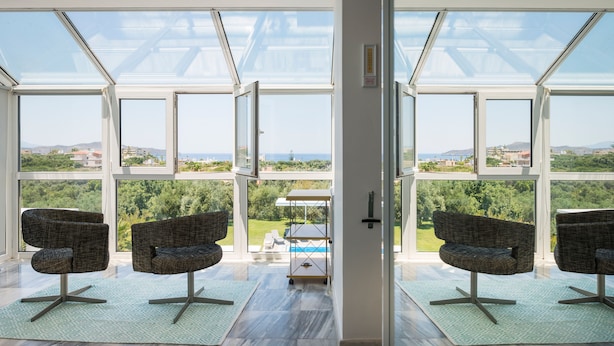 A spacious room with large windows offering a view of a pool and greenery. There are two upholstered chairs and a small table. - Stunning villa for private Escape/ Create priceless memories! large private pool (Hania)