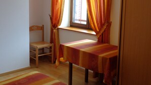 A small room with a wooden chair, a table with a patterned tablecloth, and orange curtains.
