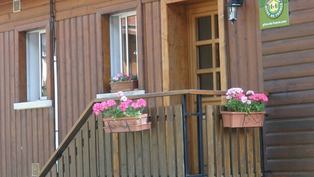 A wooden building with a wooden fence, a wooden door, and a window. There are flower boxes on the fence.