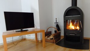 A living room with a television on a wooden table, a black fireplace with visible flames, and a wicker basket with logs.