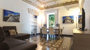 Een woonkamer met een bruine bank, een eettafel met stoelen, een tv-meubel en decoratieve wandkunst.