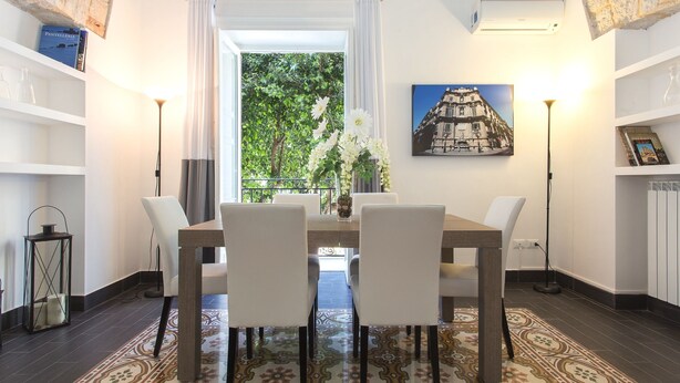 Een eethoek met een tafel en stoelen, een vloerkleed met een patroon en uitzicht op groen.