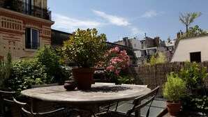 A round wooden table with chairs, surrounded by potted plants and a wooden fence. - CHARMING, AIR-CONDITIONED HOUSE WITH ROOFTOP, PARIS, CANAL ST. MARTIN (Paris)