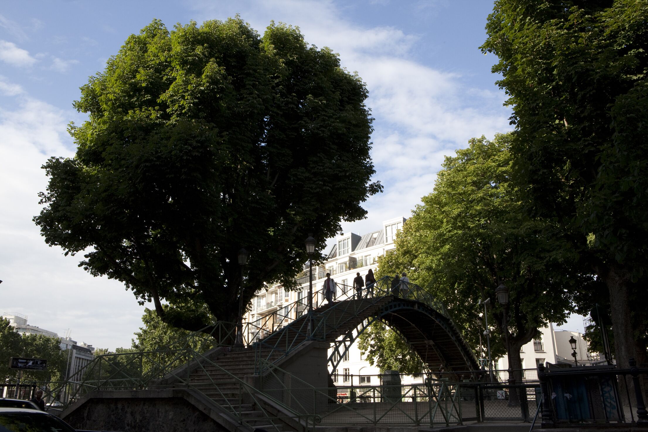 A stone bridge with an arch, surrounded by trees and buildings.