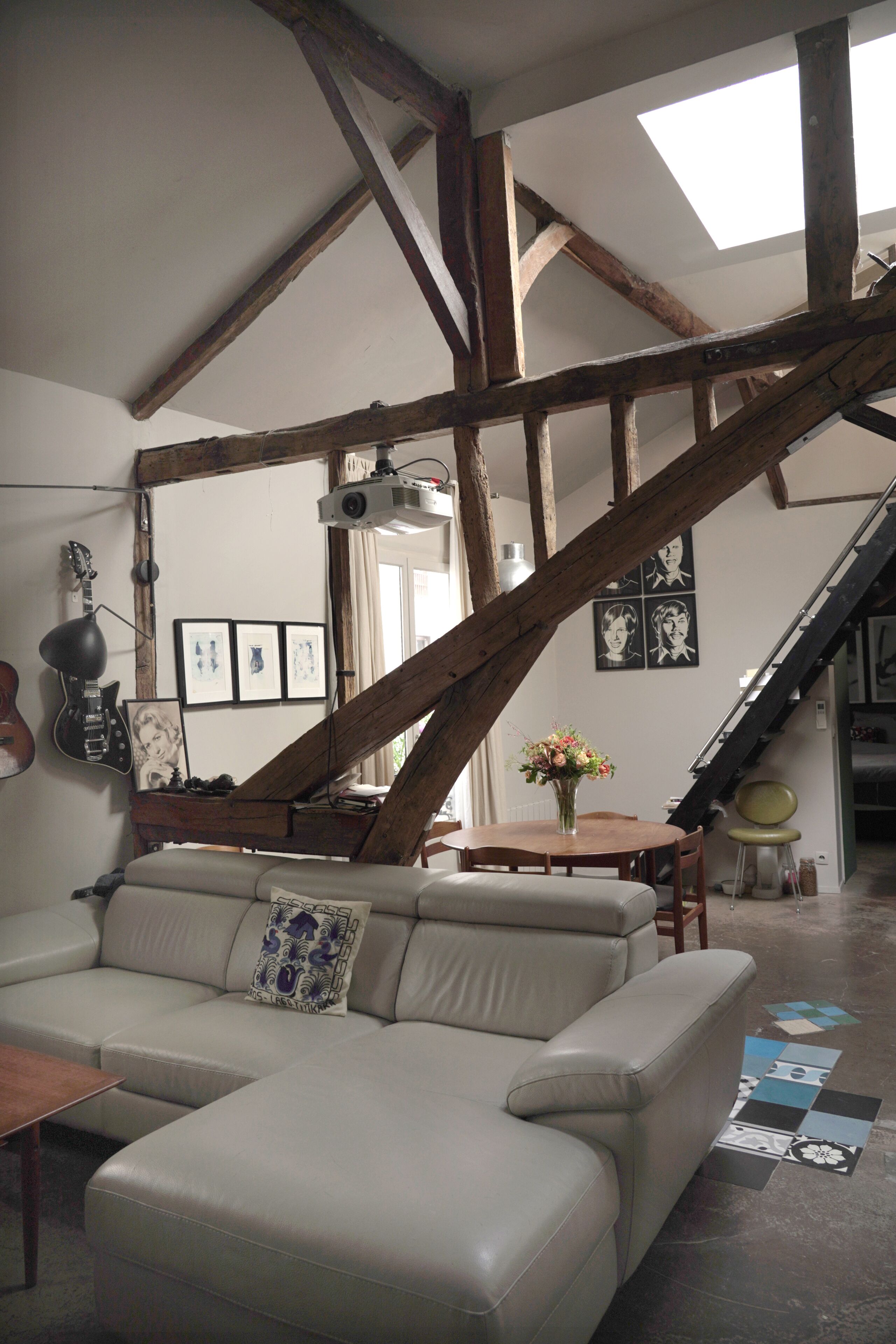 Une pièce avec un plafond haut, des poutres apparentes, un canapé, une table, une chaise, un piano et un escalier.
