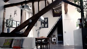 A cozy living room with exposed wooden beams, a white sofa, a wooden dining table, and a staircase leading to another level. - CHARMING, AIR-CONDITIONED HOUSE WITH ROOFTOP, PARIS, CANAL ST. MARTIN (Paris)