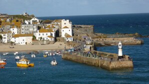 Un pueblo costero con un faro, un puerto con barcos y edificios a lo largo de la orilla.