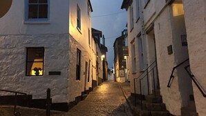 Una estrecha calle adoquinada bordeada por edificios blancos con ventanas y puertas visibles, que conduce a una escalera.