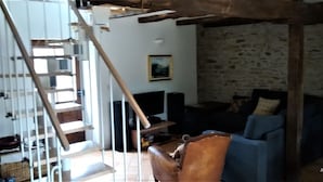 A staircase with a wooden handrail leading to a landing. There is a stone wall with a framed picture above a dark-colored sofa. - NEW: Barn conversion in a fantastic village in the Lot (Limogne-en-Quercy)