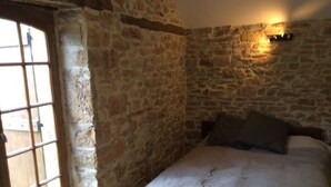 A room with a stone wall, a bed with a white duvet, and a window with a view of the outside. - NEW: Barn conversion in a fantastic village in the Lot (Limogne-en-Quercy)