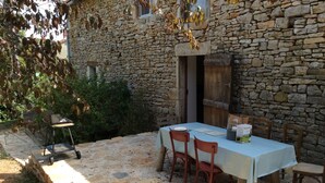 A stone building with a table set for two, surrounded by chairs, and a small cart with a grill. - NEW: Barn conversion in a fantastic village in the Lot (Limogne-en-Quercy)