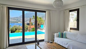 Une pièce avec un canapé blanc, une table basse en bois et une vue sur une piscine et des montagnes.