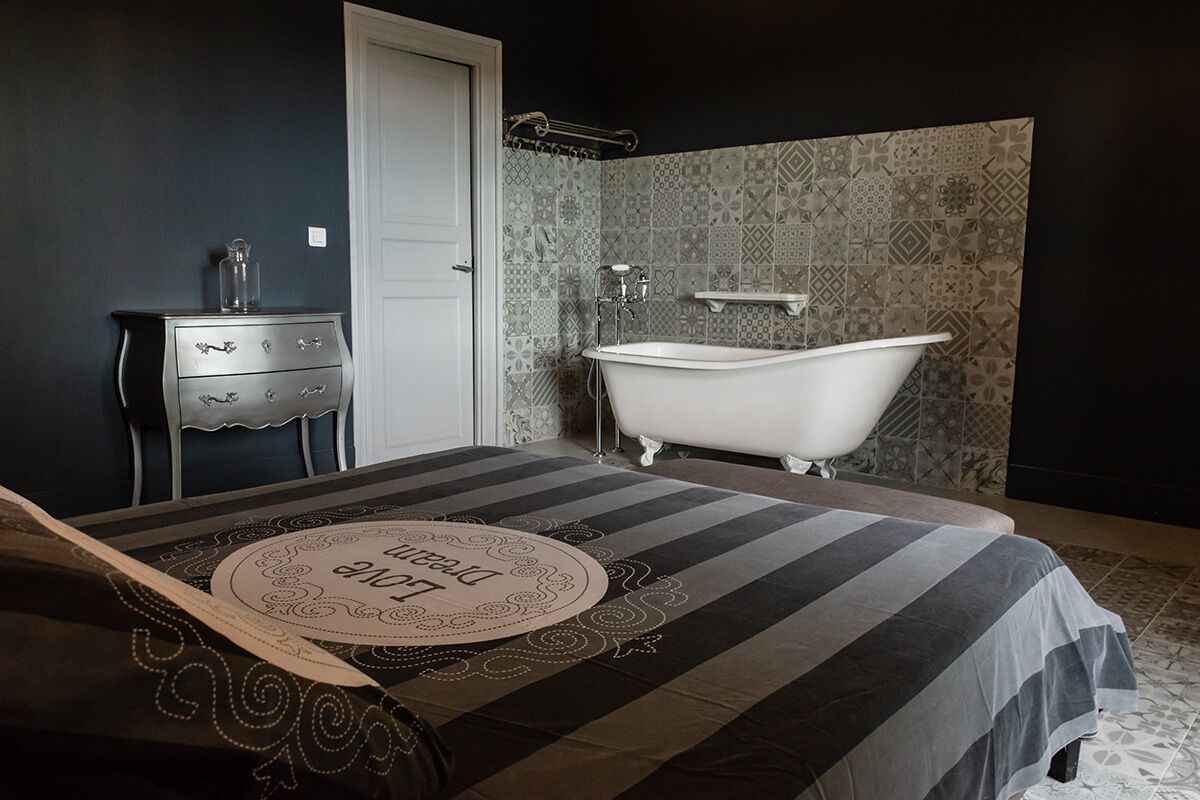 A bedroom with a bed, a dresser, a vanity, and a white clawfoot bathtub.