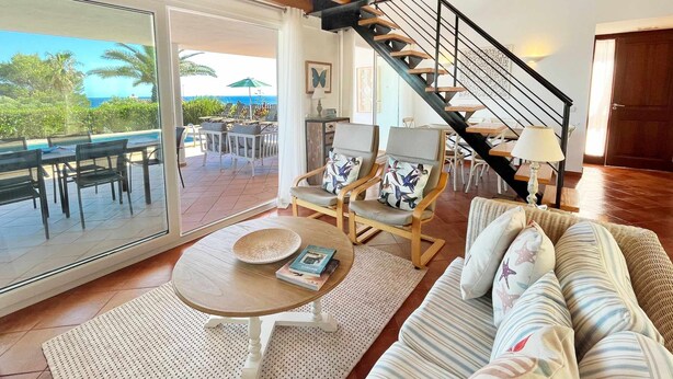 Un'ampia zona giorno con divano, poltrone, tavolo e una scala che conduce a un patio esterno con vista sull'oceano.